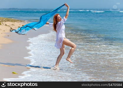 The young attractive woman jumping with a blue scarf in hands