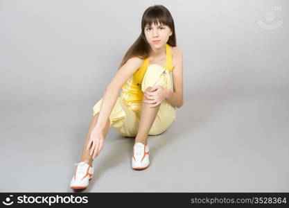 The young beautiful girl in a yellow vest and sports footwear on a grey background