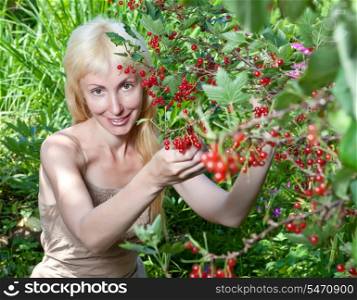 The young beautiful girl near to a bush of a red currant.