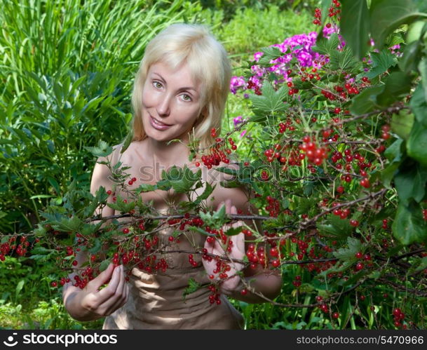 The young beautiful girl near to a bush of a red currant.