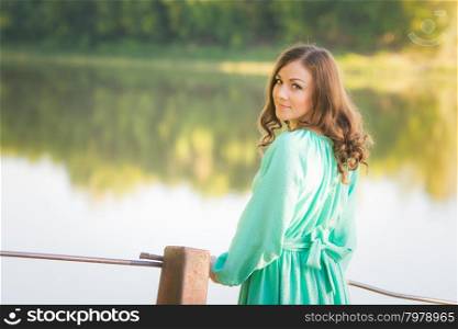 The young beautiful girl walks on an old bridge in the warm autumn weather. A girl standing on a bridge over the river turned and looked into the frame