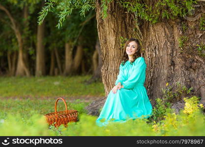 The young beautiful girl walks through the forest on a warm summer day. A girl in a long dress sat by a tree in the woods