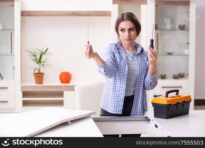 The young beautiful woman assembling furniture at home. Young beautiful woman assembling furniture at home