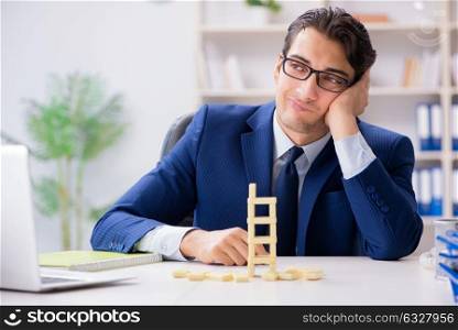 The young businessman building domino tower in office. Young businessman building domino tower in office