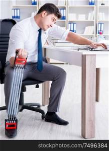 The young businessman exercising with elastic expander in office. Young businessman exercising with elastic expander in office