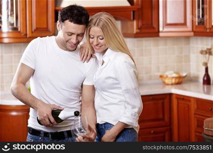 The young couple pours champagne in kitchen