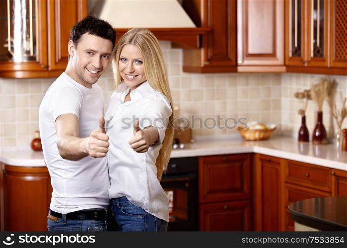 The young couple shows thumbs upwards on kitchen