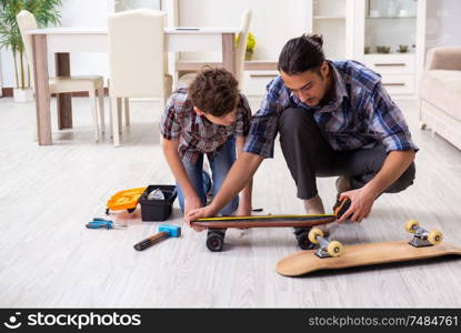 The young father repairing skateboard with his son at home. Young father repairing skateboard with his son at home