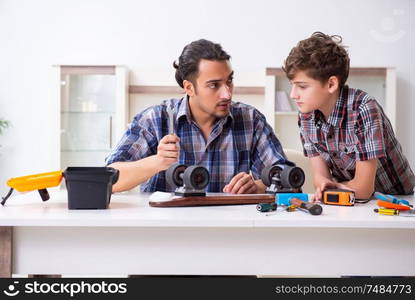 The young father repairing skateboard with his son at home. Young father repairing skateboard with his son at home