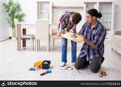 The young father repairing skateboard with his son at home. Young father repairing skateboard with his son at home