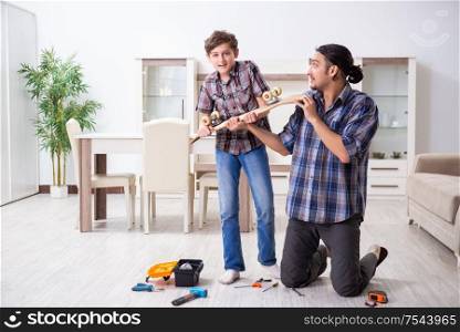 The young father repairing skateboard with his son at home. Young father repairing skateboard with his son at home