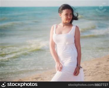 The young girl enjoys good windy weather on sea beach. Woman is dressed in white sundress and boho jewelry rest at the sea. Carefree and freedom concept. Portrait of gypsy lady.