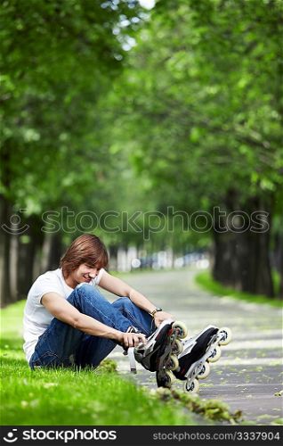 The young guy fastens rollers on a grass in park