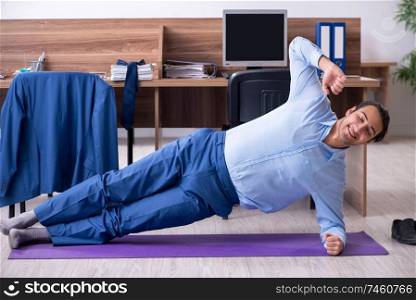 The young handsome businessman doing exercises at workplace . Young handsome businessman doing exercises at workplace 