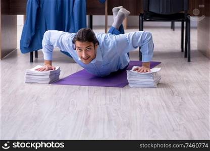 The young handsome businessman doing exercises at workplace . Young handsome businessman doing exercises at workplace 