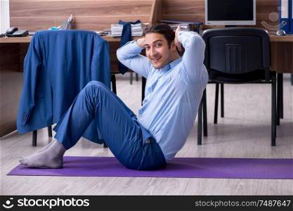 The young handsome businessman doing exercises at workplace . Young handsome businessman doing exercises at workplace