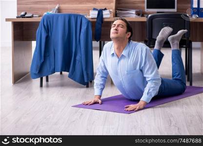 The young handsome businessman doing exercises at workplace . Young handsome businessman doing exercises at workplace