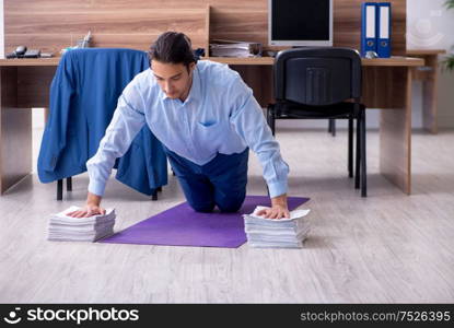 The young handsome businessman doing exercises at workplace. Young handsome businessman doing exercises at workplace