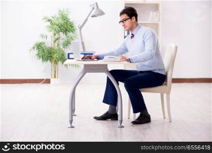 The young handsome businessman employee working in office at desk. Young handsome businessman employee working in office at desk. The young handsome businessman employee working in office at desk