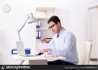 The young handsome businessman employee working in office at desk. Young handsome businessman employee working in office at desk. The young handsome businessman employee working in office at desk