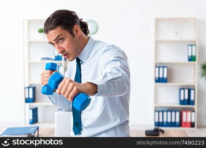 The young handsome employee doing sport exercises at workplace. Young handsome employee doing sport exercises at workplace