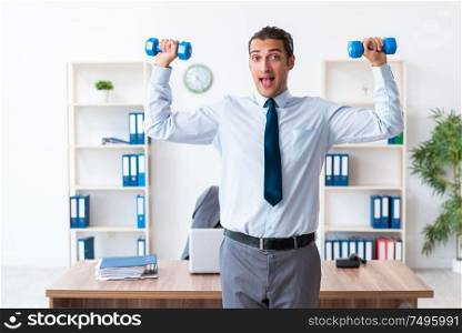 The young handsome employee doing sport exercises at workplace. Young handsome employee doing sport exercises at workplace