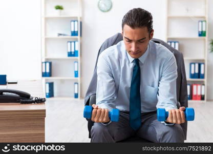 The young handsome employee doing sport exercises at workplace. Young handsome employee doing sport exercises at workplace