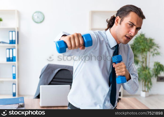 The young handsome employee doing sport exercises at workplace. Young handsome employee doing sport exercises at workplace