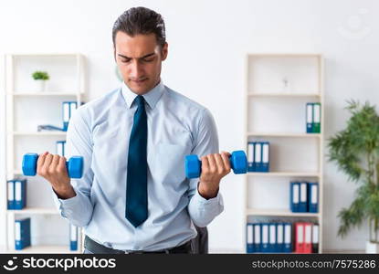 The young handsome employee doing sport exercises at workplace. Young handsome employee doing sport exercises at workplace