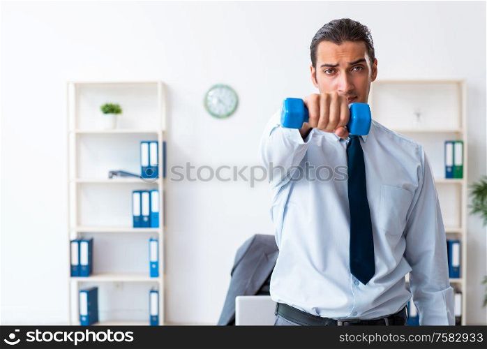 The young handsome employee doing sport exercises at workplace. Young handsome employee doing sport exercises at workplace