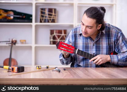 The young handsome repairman repairing guitar. Young handsome repairman repairing guitar