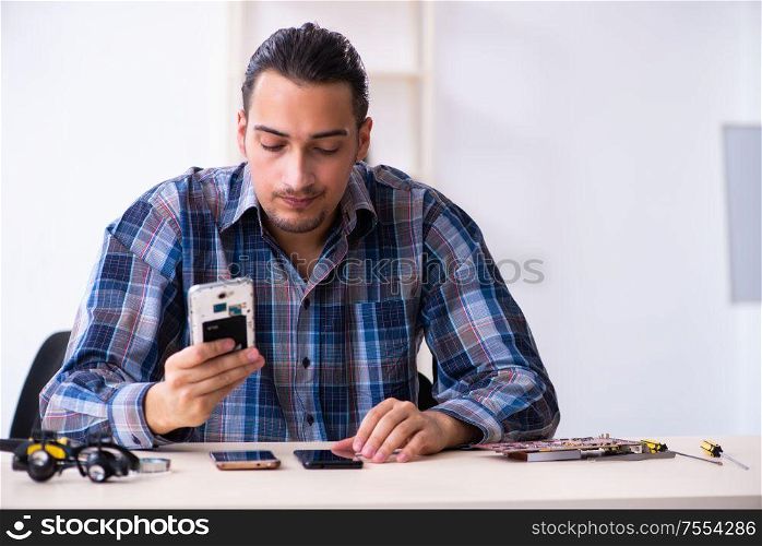 The young handsome technician repairing mobile phone. Young handsome technician repairing mobile phone