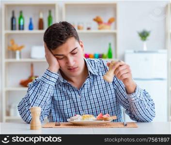 The young husband eating tasteless food at home for lunch. Young husband eating tasteless food at home for lunch