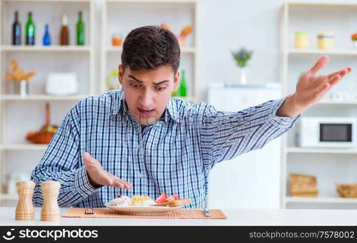 The young husband eating tasteless food at home for lunch. Young husband eating tasteless food at home for lunch