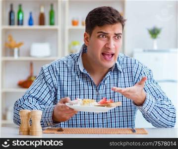 The young husband eating tasteless food at home for lunch. Young husband eating tasteless food at home for lunch