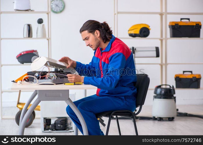 The young male contractor repairing air-conditioner at workshop. Young male contractor repairing air-conditioner at workshop