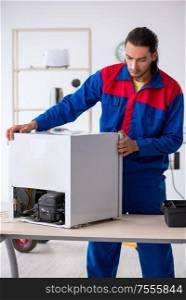 The young male contractor repairing refrigerator at workshop. Young male contractor repairing refrigerator at workshop