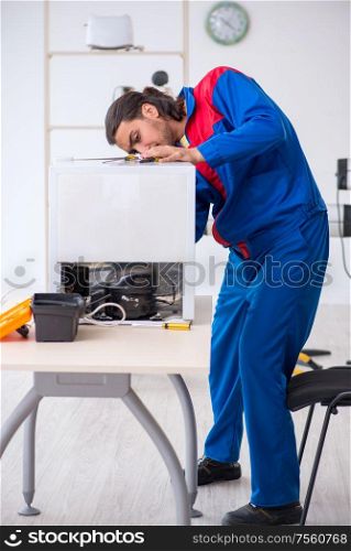 The young male contractor repairing refrigerator at workshop. Young male contractor repairing refrigerator at workshop