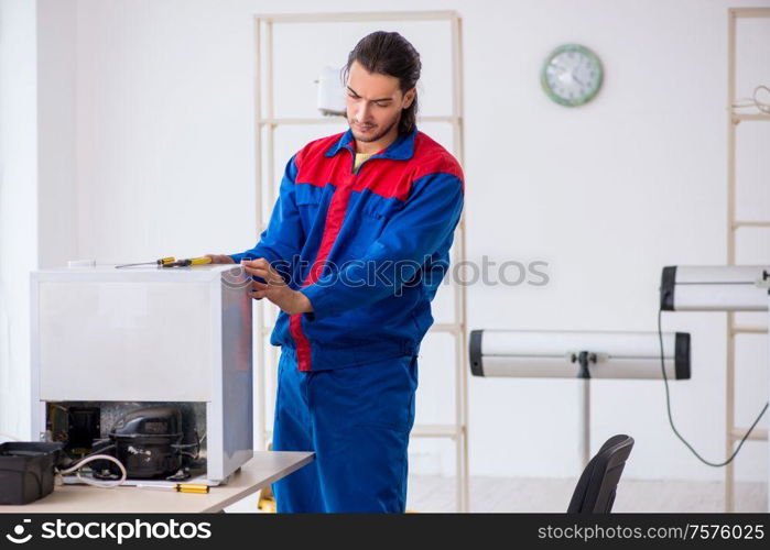 The young male contractor repairing refrigerator at workshop. Young male contractor repairing refrigerator at workshop