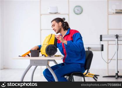 The young male contractor repairing vacuum cleaner at workshop. Young male contractor repairing vacuum cleaner at workshop