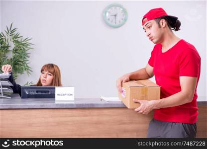 The young male courier delivering box to hotel&rsquo;s reception. Young male courier delivering box to hotel&rsquo;s reception