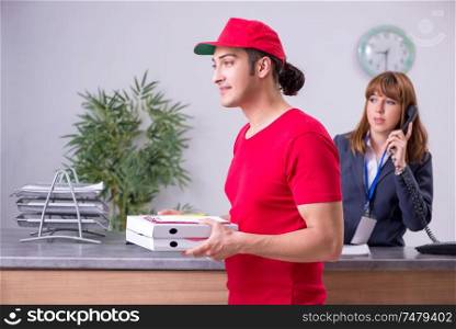The young male courier delivering pizza to hotel&rsquo;s reception . Young male courier delivering pizza to hotel&rsquo;s reception
