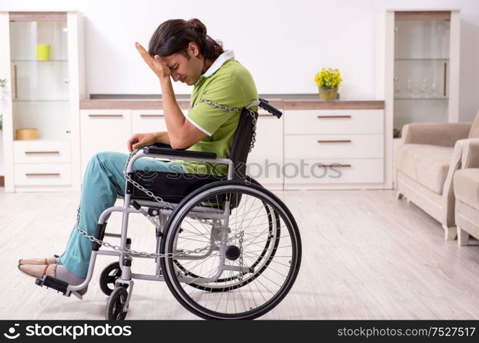 The young male invalid in wheel-chair suffering at home. Young male invalid in wheel-chair suffering at home