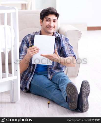 The young man assembling baby bed with instruction manual. Young man assembling baby bed with instruction manual