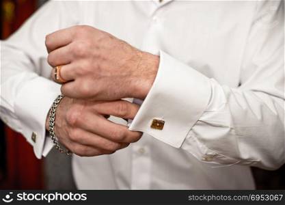 The young man clasps a cuff link on a shirt.
