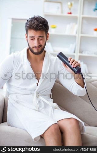 The young man drying hair at home with a hair dryer blower . Young man drying hair at home with a hair dryer blower