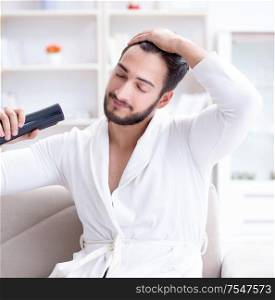The young man drying hair at home with a hair dryer blower. Young man drying hair at home with a hair dryer blower
