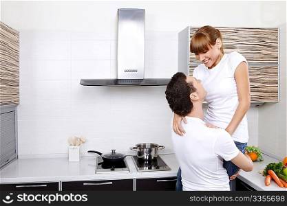 The young man holds the smiling girl at kitchen