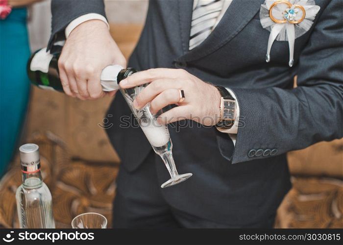 The young man in a suit pours champagne in a glass.. The man pours wine in a glass.