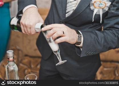 The young man in a suit pours champagne in a glass.. The man pours wine in a glass.
